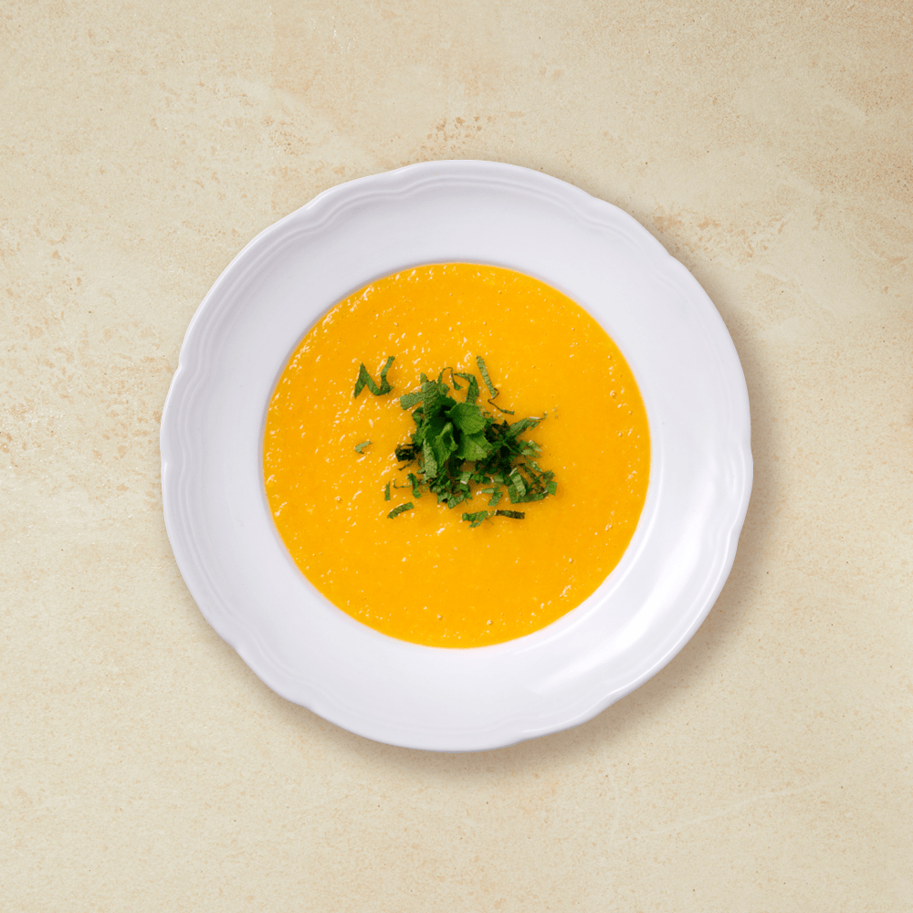 Kald mango- og melonsuppe i oransje, servert i hvit suppeskål med hakket mynte over.