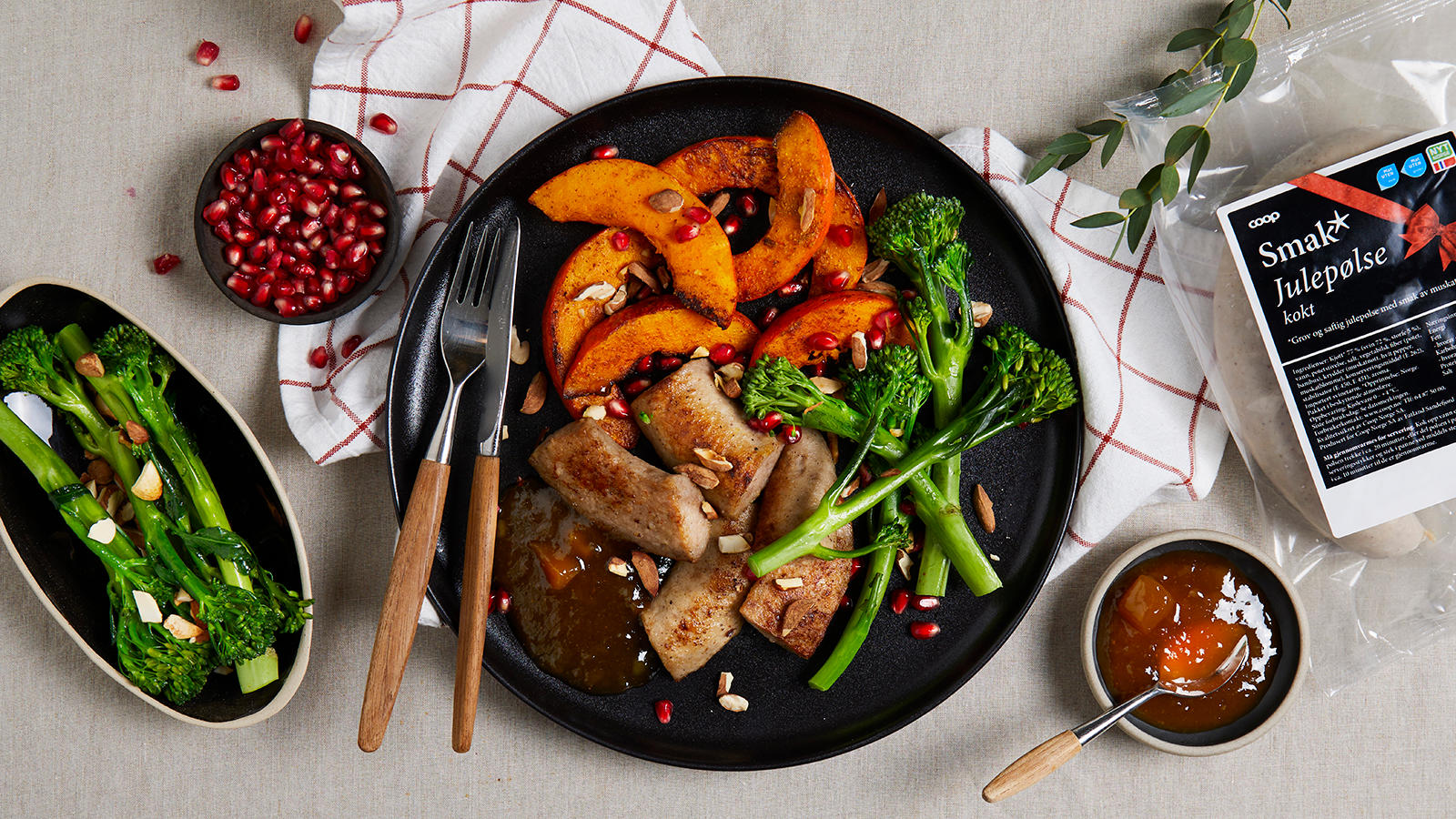 Julepølse med currykrydret gresskar og hvitløkstekt brokkolini servert på svart tallerken med mangochutney, granateplekjerner og skivede mandler.