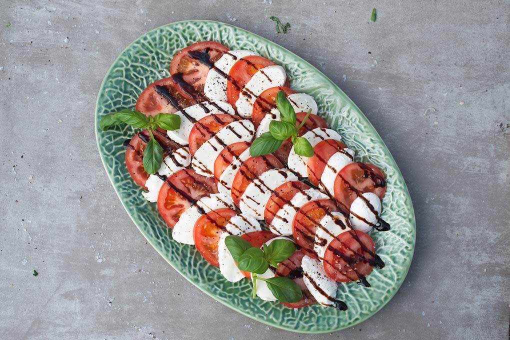 Caprese av mozzarella, tomat, fersk basilikum og balsamico servert på grønt avlangt fat.