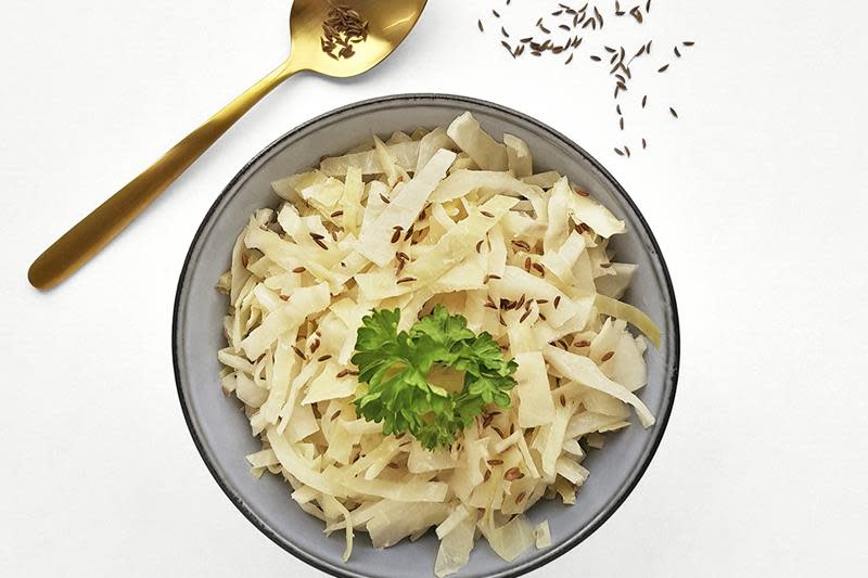 Hjemmelaget surkål i grå keramikkbolle, med gullskje ved siden av. Surkålen er pyntet med karve og fersk bladpersille.