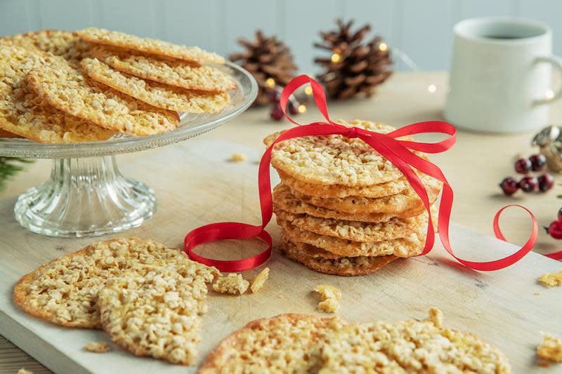 Gylne sprø havreflarn lagt i stabel, og bundet sammen med rødt bånd. Julepyntet bord med kongler, kaffekopp og kakefat med havreflarn i bakgrunnen.