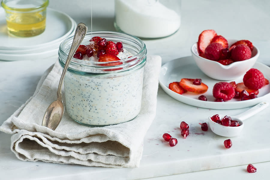 Kjøleskapsgrøt med chiafrø, kanel og vanilje servert i syltetøyglass på marmorfjøl med linserviett. Grøten er toppet med jordbær, bringebær og granateplefrø, og honning blir ringlet over. Liten skål med ferske bær i bakgrunnen.