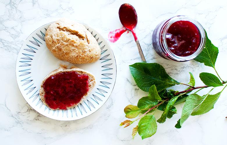 Glass med hjemmelaget plommesyltetøy, servert på nystekt rundstykke.