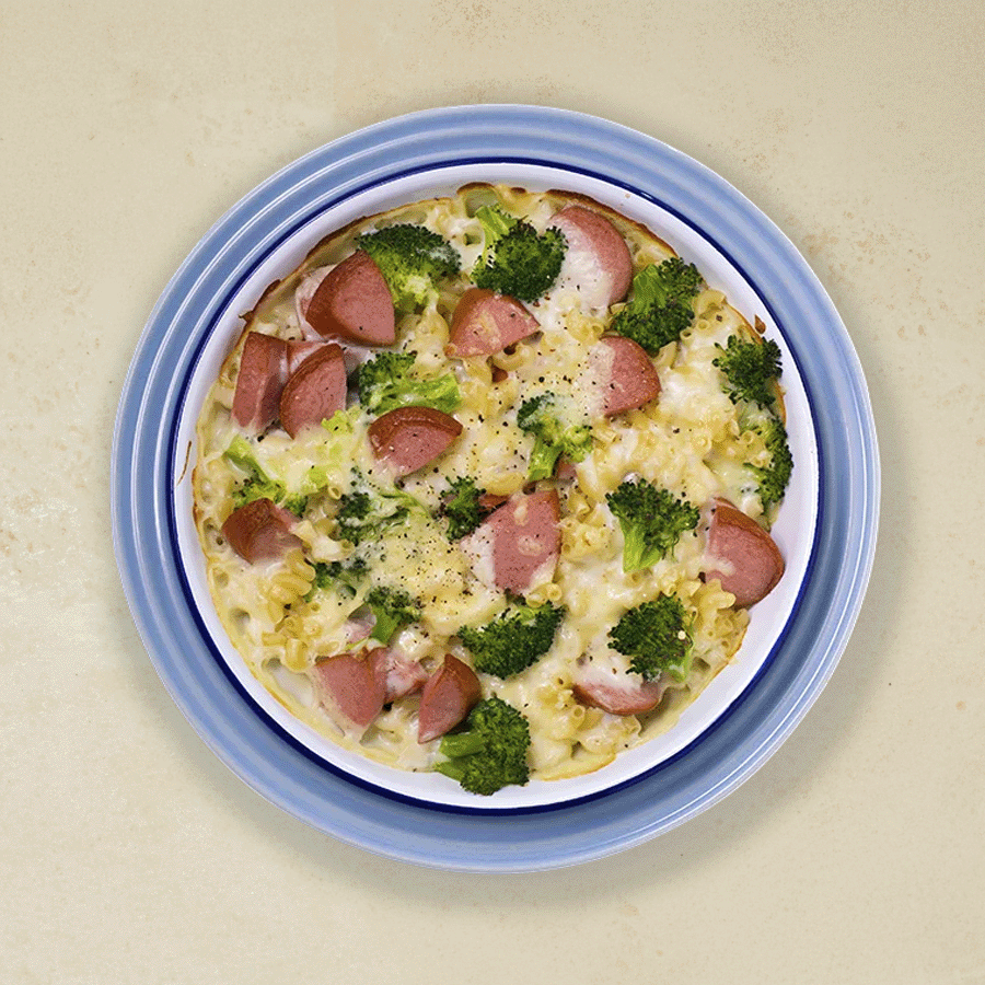 Brokkoligrateng med makaroni og pølsebiter, servert i en skål med blå kant.