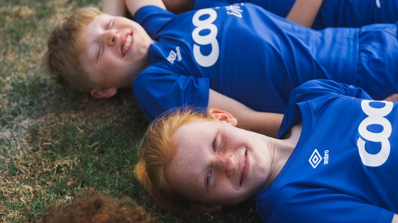Tre barn med fotballdrakt på fotballbane.