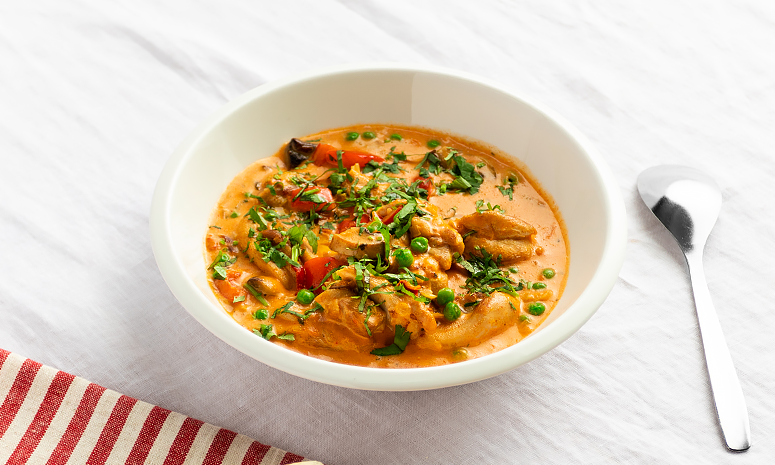 Kyllinggryte med paprika og sopp servert i en dyp hvit skål med en skje liggende på høyre side, alt ligger på en hvit duk