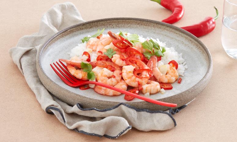 Spicy scampi med chili, hvitløk og ris, på lys grå tallerken med rød gaffel. Fersk koriander på toppen. Lys bakgrunn.