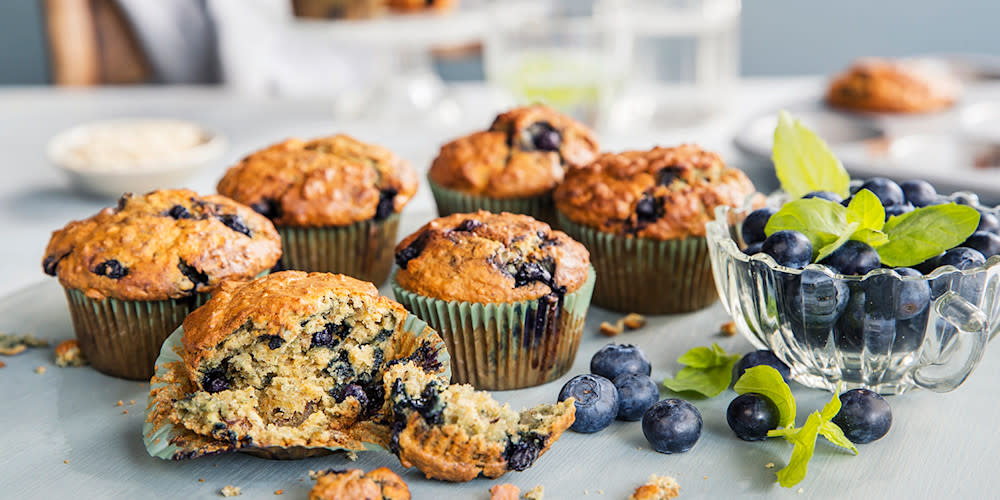 Saftige blåbærmuffins med vaniljekesam i deigen, servert på dekket bord med skål med store blåbær ved siden av.