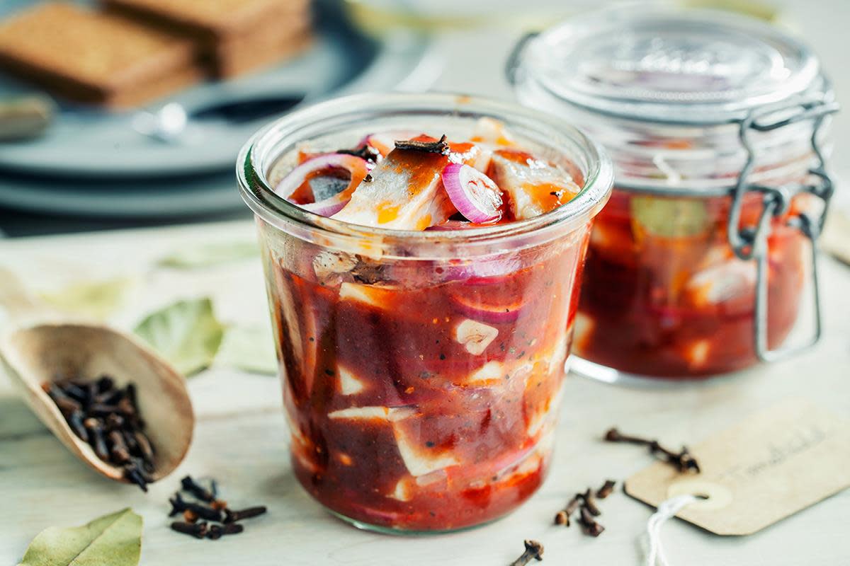 Tomatsild til jul fylt på to Norgesglass med nellik, laurbærblad og rødløk. Glassene står på trefjøl med tørkede krydder rundt, og en gavelapp som kan festes på glasset.