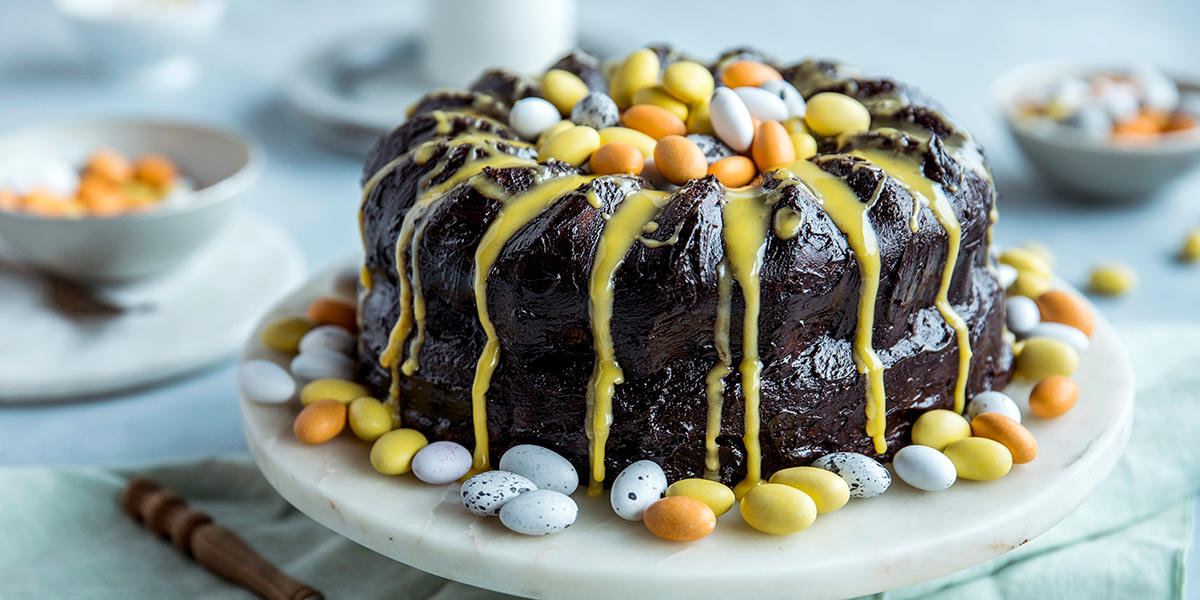 Appelsinkake med mørk sjokoladekrem pyntet med gul appelsinglasur og mandelegg, servert på stettfat i marmor.