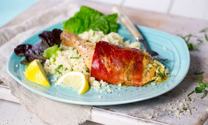 Skinkesurret kyllinglår med urter og feta, på lys blå tallerken med couscous, salat og sitronbåter.