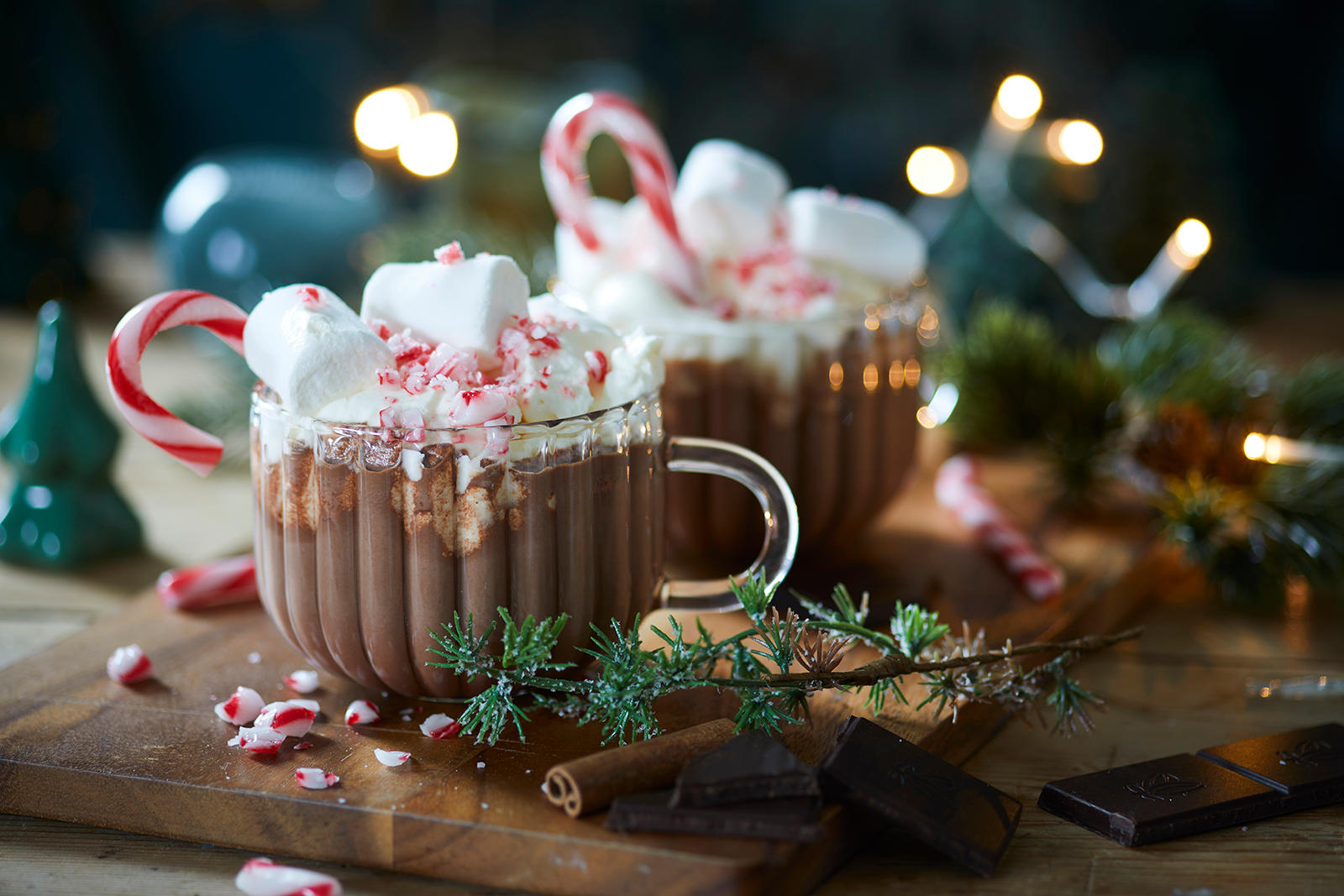 Hjemmelaget kakao med peppermynte servert i glasskrus på trefjøl, og pyntet med pisket krem, polkastenger, knuste polkagriser og marshmallows.