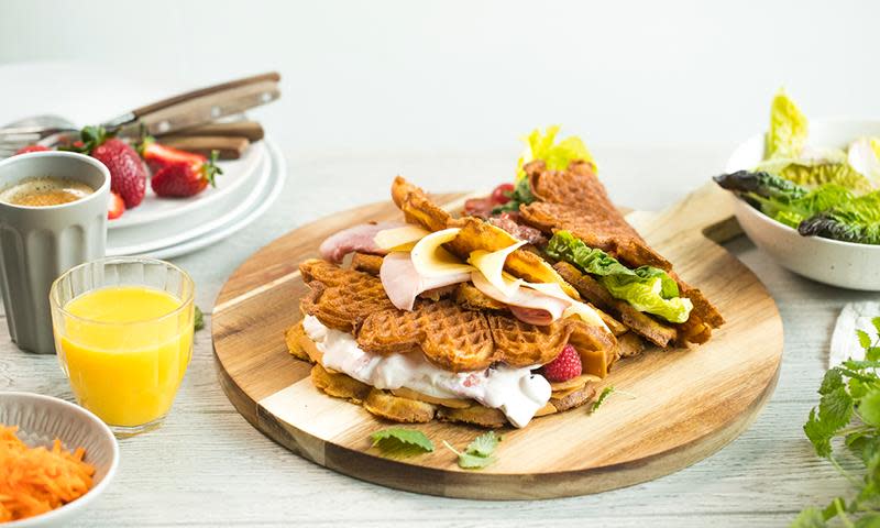 Sunnere frokostvafler med havremel i røren, lagt på rund trefjøl og fylt med tre forskjellige fyll. Frokostbord med juiceglass, kaffekopp og salat ved siden av.