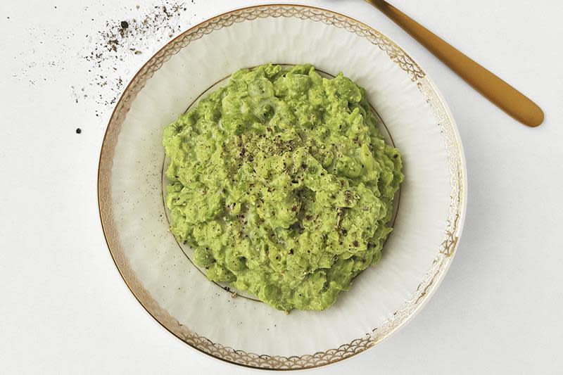 Grønn kremet ertestuing i gullkantet hvit skål, toppet med kvernet pepper.