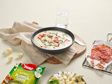 Blomkålsuppe med sprøstekt spekeskinke på siden og grønnsaker på en tallerken og Toro blomkålsuppe pose i forgrunnen