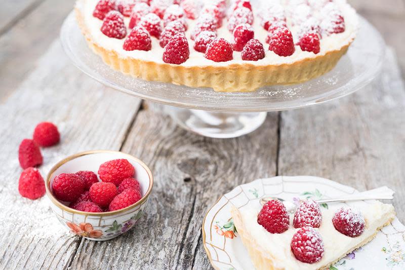 Utsnitt av bringebærterte med kremostfyll og ferske bringebær på toppen, på stettfat. Rustikk trebakgrunn.