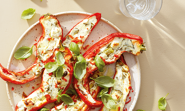 Halve avlange grillet paprika med fetakrem. Paprikaen ligger på hvit tallerken, med fersk basilikum strødd over.