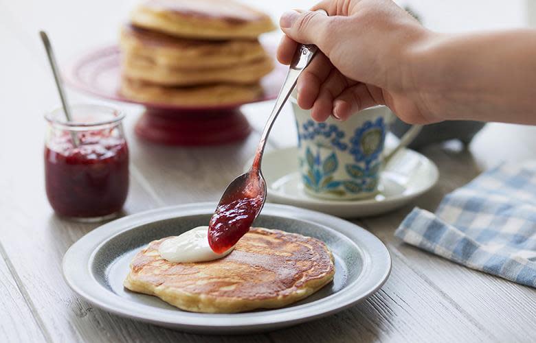 Hjemmelagede gyldne sveler, servert med rømme og rødt syltetøy. Blårutete kjøkkenhåndkle ved siden av.