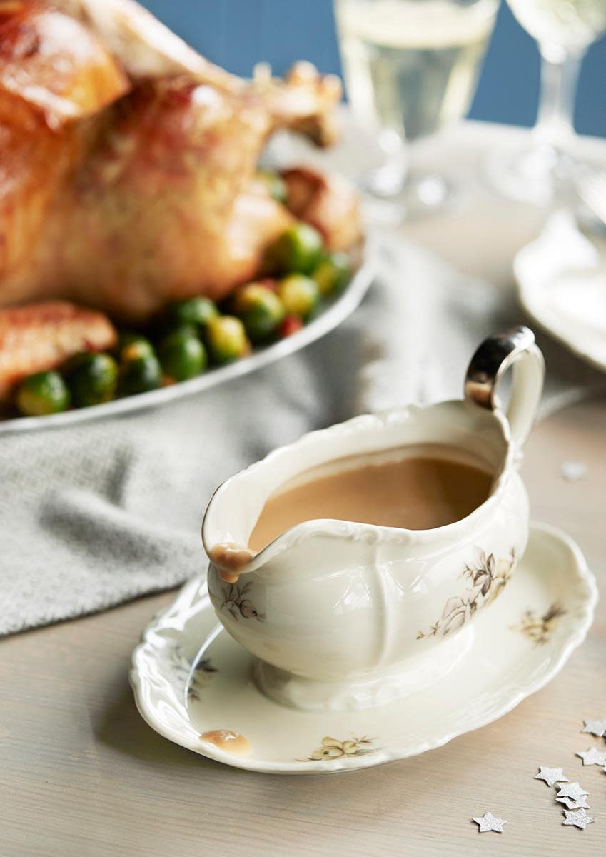 Fløtesaus til kalkun servert i lyst sausenebb med blomsterdetaljer. I bakgrunnen står det en helstekt kalkun på et festpyntet bord.