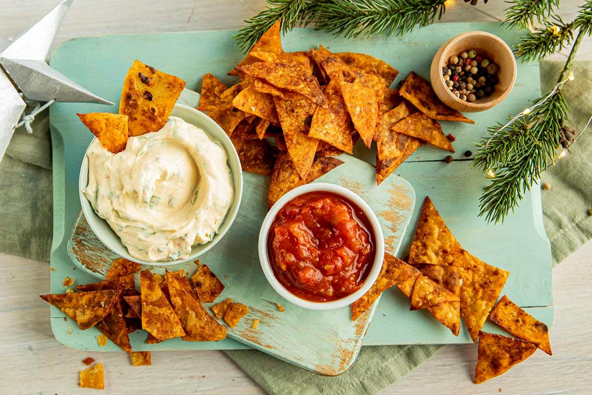 Lompechips og dip servert på lyseblå trefjøl med skåler med Holiday dip og salsa. Granbar og julepynt rundt.