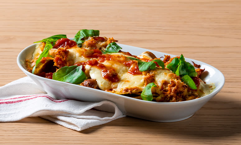 Nachos med pulled chicken og revet ost i en hvit form pyntet med basilikum.