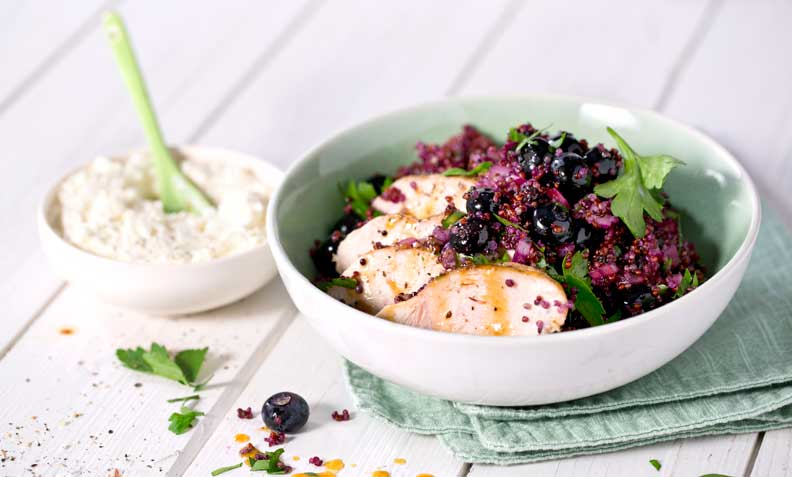 Stekt kyllingbryst med quinoasalat med blåbær, og fetakrem i lys grønn skål. Hvit trebakgrunn.
