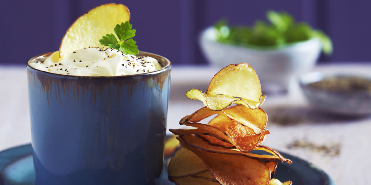 Hjemmelaget potetgull med trøffeldipp servert på blå asjett, med dipp i et blått keramikk krus. Bolle med friske urter i bakgrunnen.