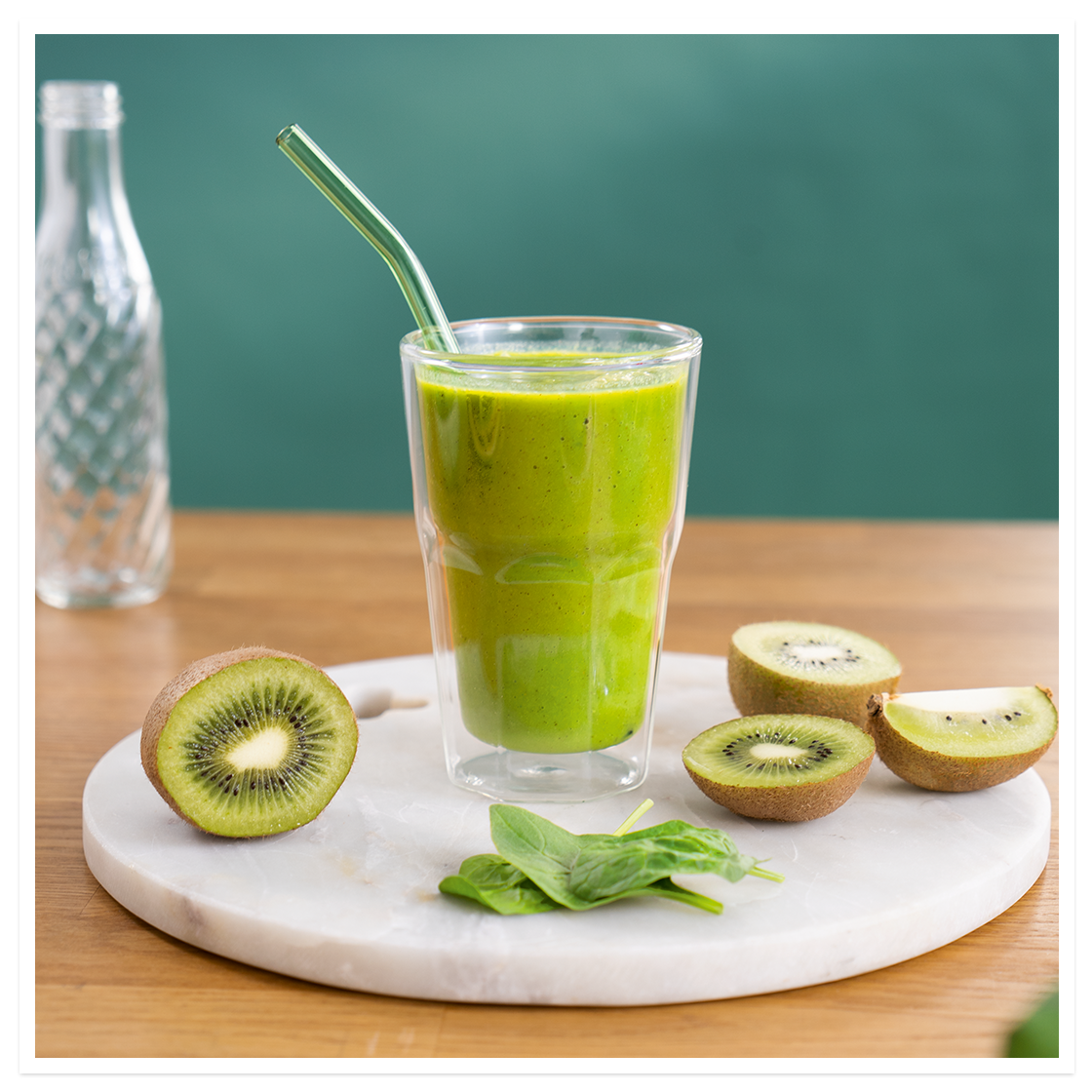 Jungelgrønn smoothie, grønn smoothie med kiwi, mango, kokos og spinat, i glass på hvit marmorfjøl. Fersk kiwi og spinat ved siden av.