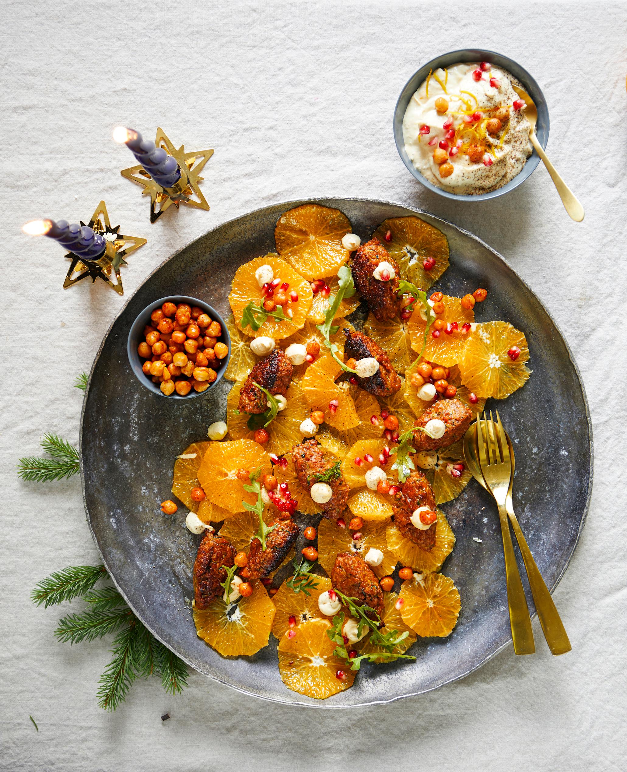 Vegetarfrikadeller med hummus og appelsinsalat, krydrede kikerter og granateplefrø servert på mørk tallerken på lys linduk.
