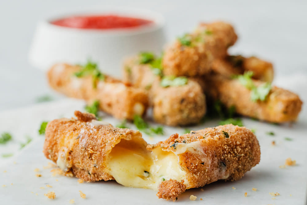 Hjemmelagede mozzarella sticks med hot tomatdipp servert på marmorplate med et dryss friske urter over.