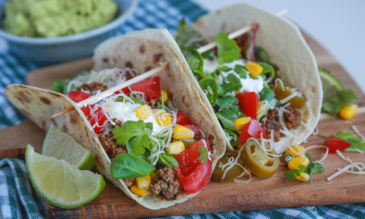 Lettere taco. To tacolefser. En laget med karbonadedeig og speltlompe, og en med kjøttdeig og tortillalefse på en skjærefjøl med limebåter.