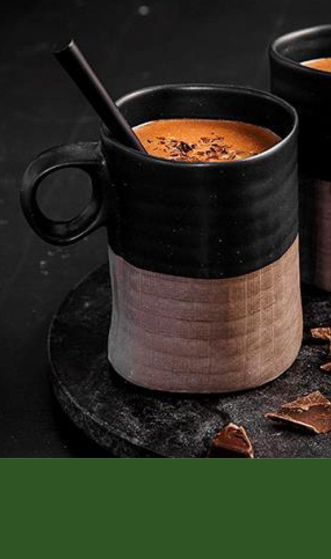 to sorte og beige keramikkopper med kakao øverst og grønn bakgrunn nederst