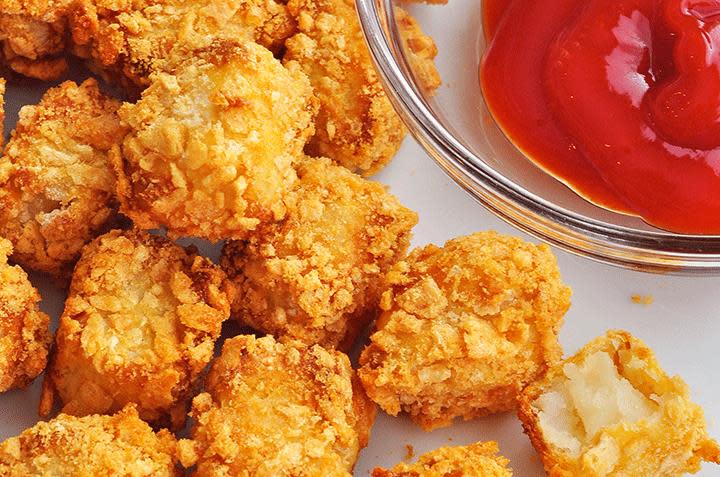 Tater tots - ovnsstekte kuler av potetmos med sprø panering, servert på hvitt underlag med en skål ketchup ved siden av.