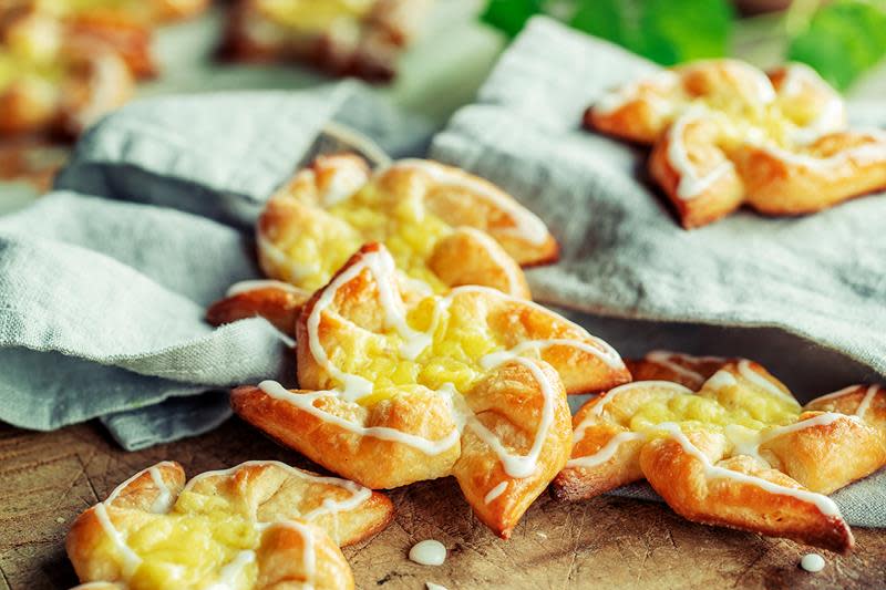 Hjemmelagede wienerbrød formet som stjerner, med vaniljekrem og melisglasur. Servert på rustikk trebord med lys grønn linserviett.