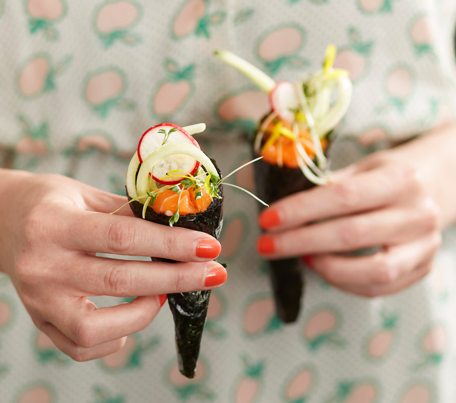 Temaki med sommerens grønnsaker, ørret og urter holdes av to kvinnehender med rød neglelakk på fingerneglene.