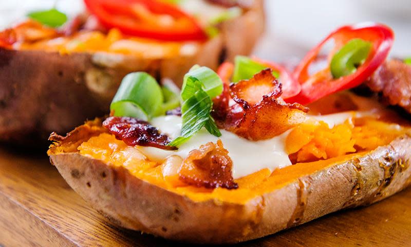 Bakt søtpotet med bacon, creme fraiche, vårløk og paprika, servert på trefjøl.