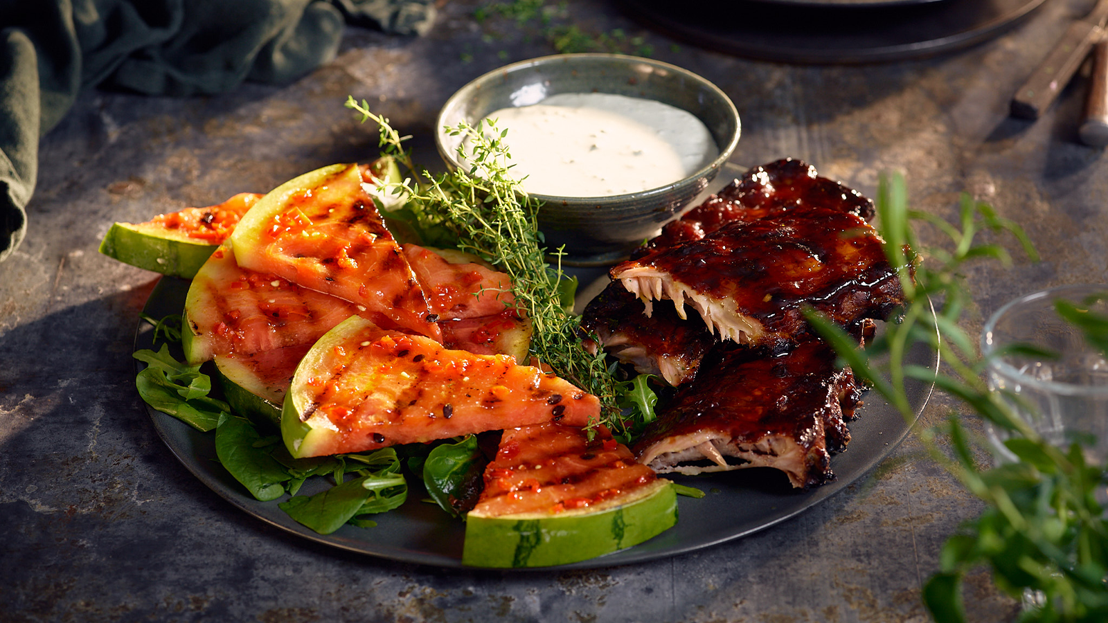 Grillet vannmelon med spareribs og blue cheese dressing servert på mørk tallerken med friske urter.