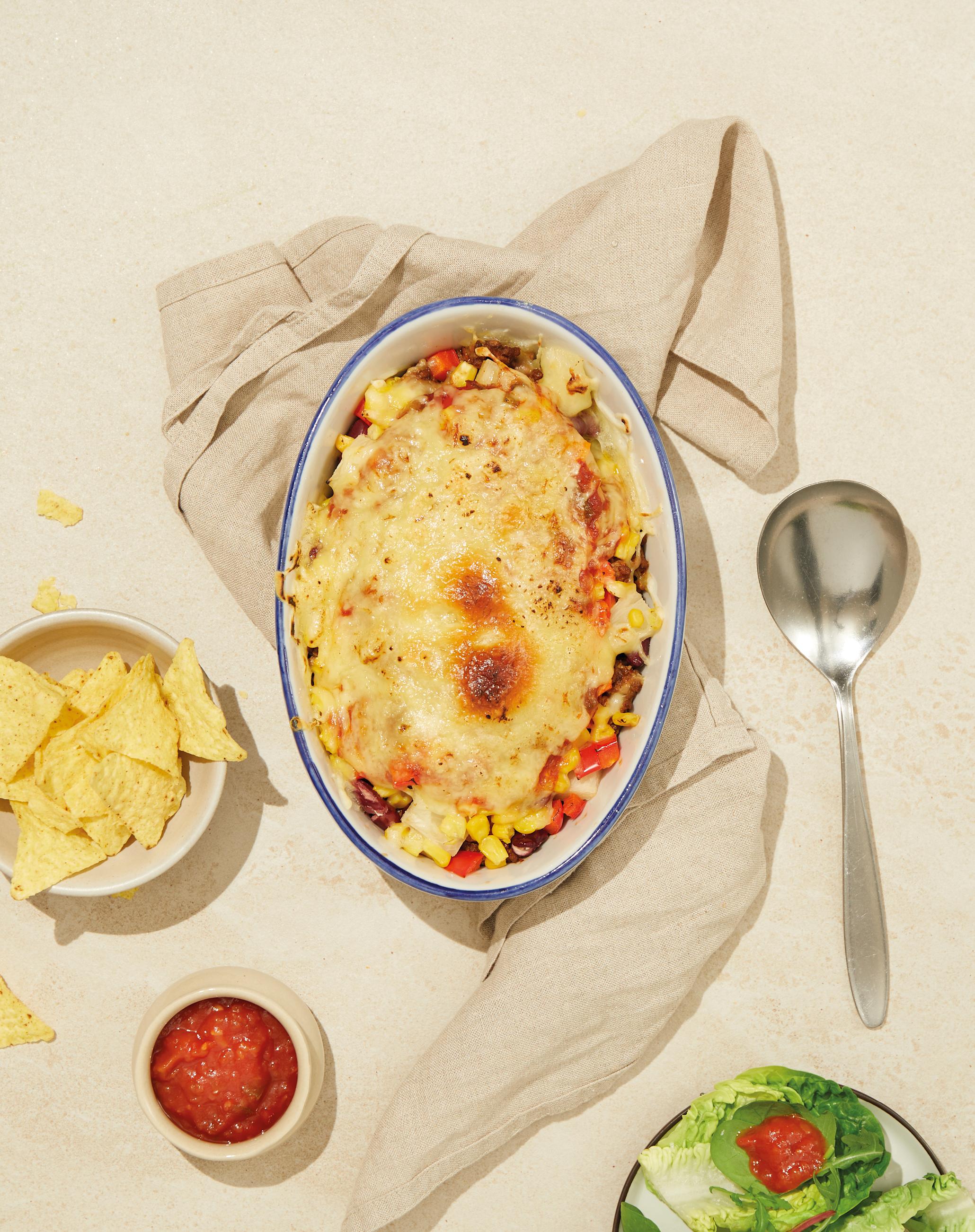 Tacograteng i hvit form på beige kjøkkenhåndkle, med salsa, salat og tortillachips ved siden av.