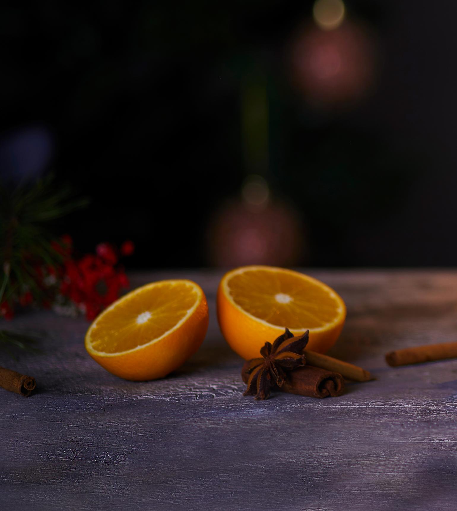 En appelsin delt i to, servert på steinbord. Tørkede krydder og tørkede røde bær strødd rundt appelsinen, og tente lys i bakgrunnen.