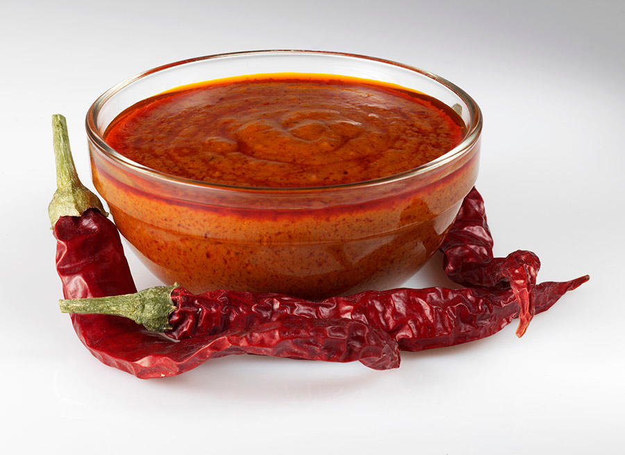 Skål med hjemmelaget chilisaus. Hel tørket chili på siden.