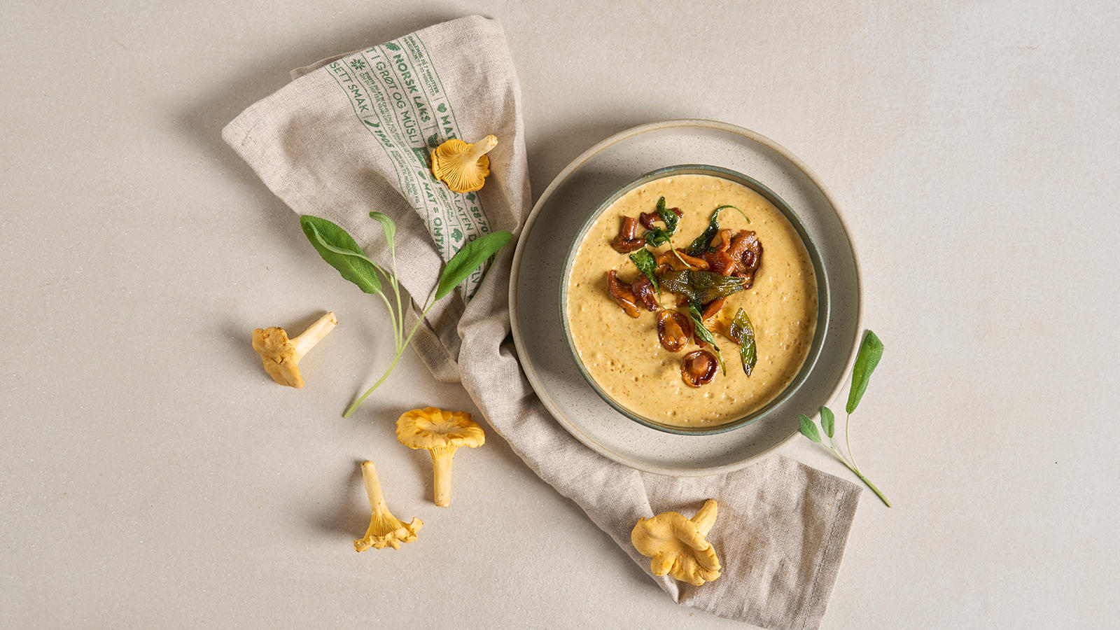 Kremet soppsuppe med kantareller, servert i keramikkbolle med frisk salvie og kantareller rundt.