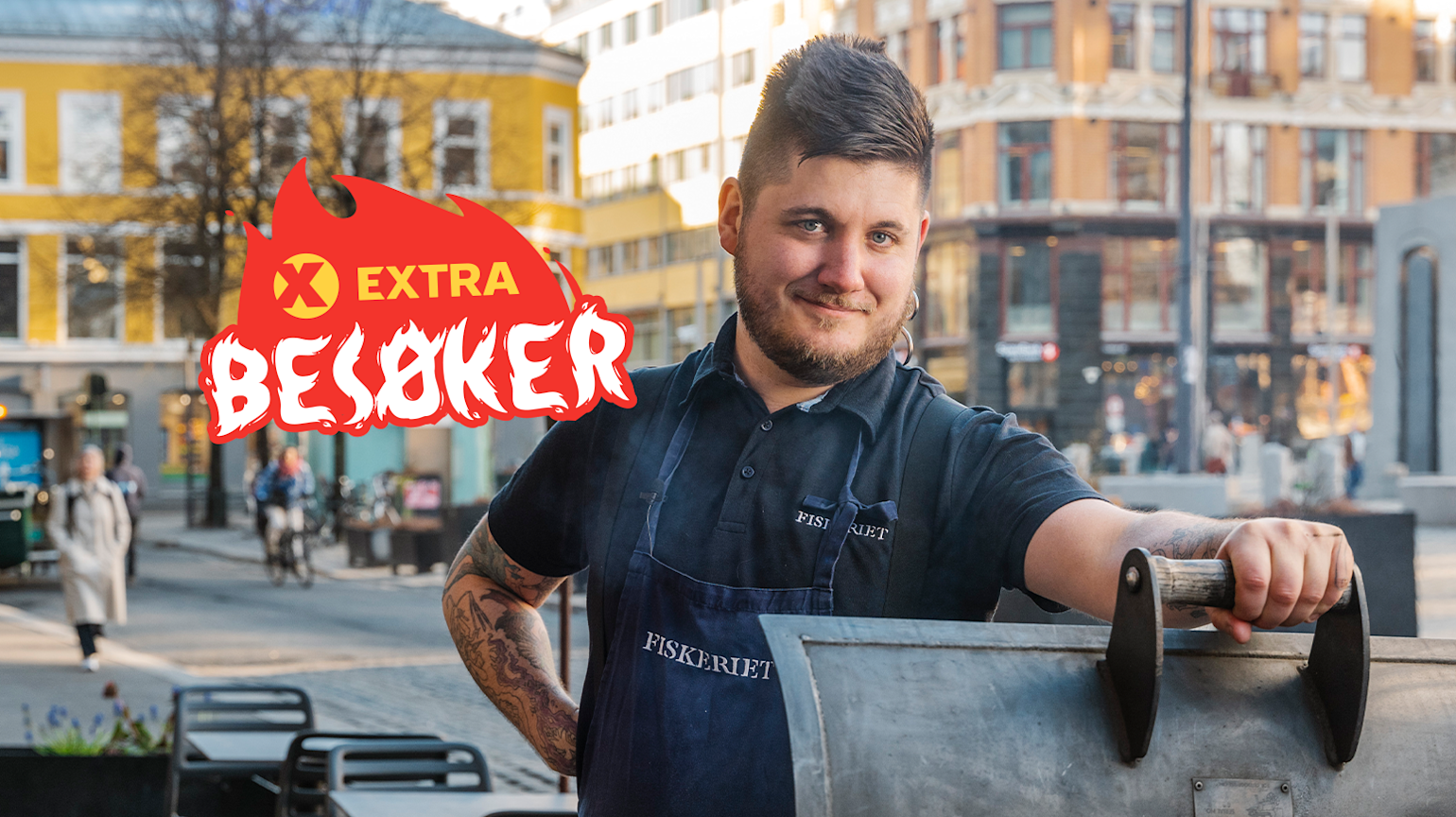 En kokk står bak en åpen grill og smiler."Extra besøker" logo er på bilde.