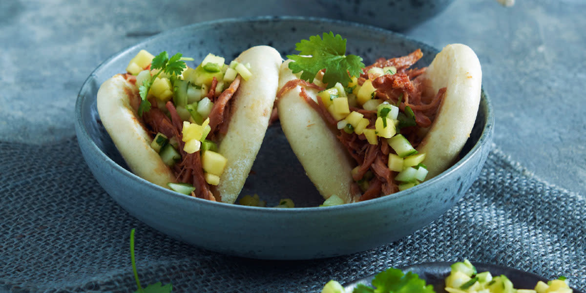 To steam buns med pulled pork og mango- og agurksalsa servert i blå bolle på blå tøyserviett. Koriander på toppen.