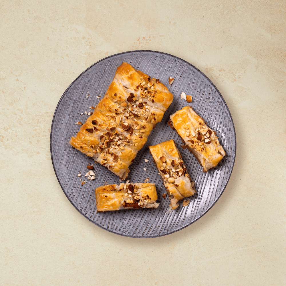 Sjokolade innbakt i butterdeig, toppet med hakkede mandler og skåret i skiver, servert på grå tallerken.