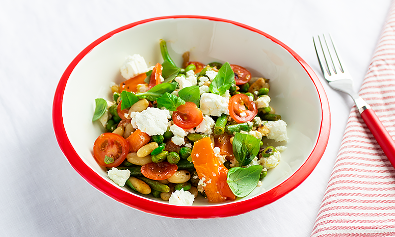 Gratinerte grønnsaker med fetaost servert i en dyp hvit skål med rød kant og en gaffel og serviett ved siden av.