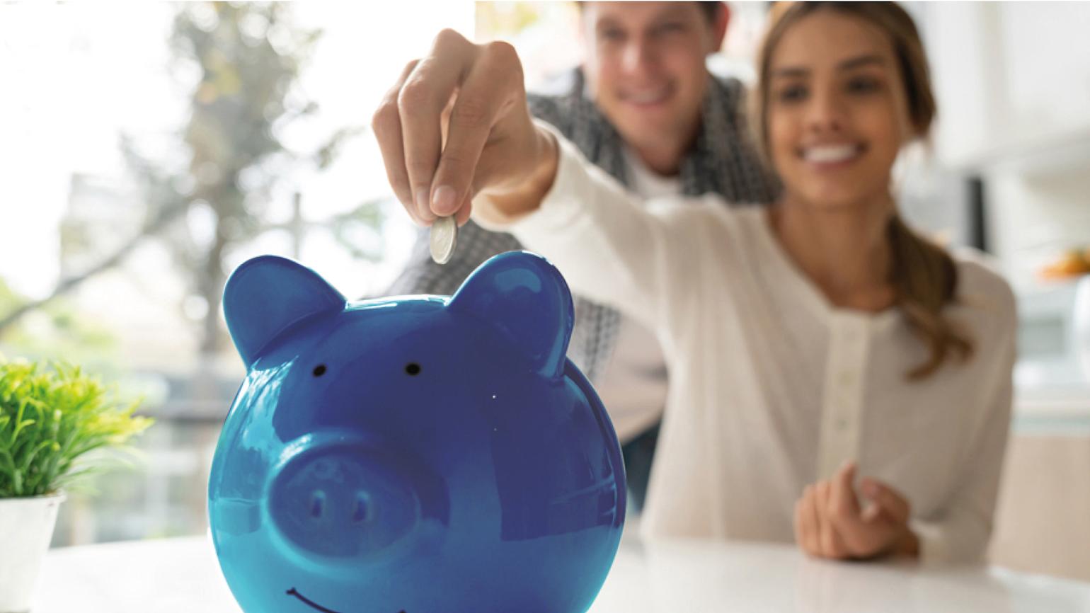 Dame putter mynter på en blå sparegris og smiler.