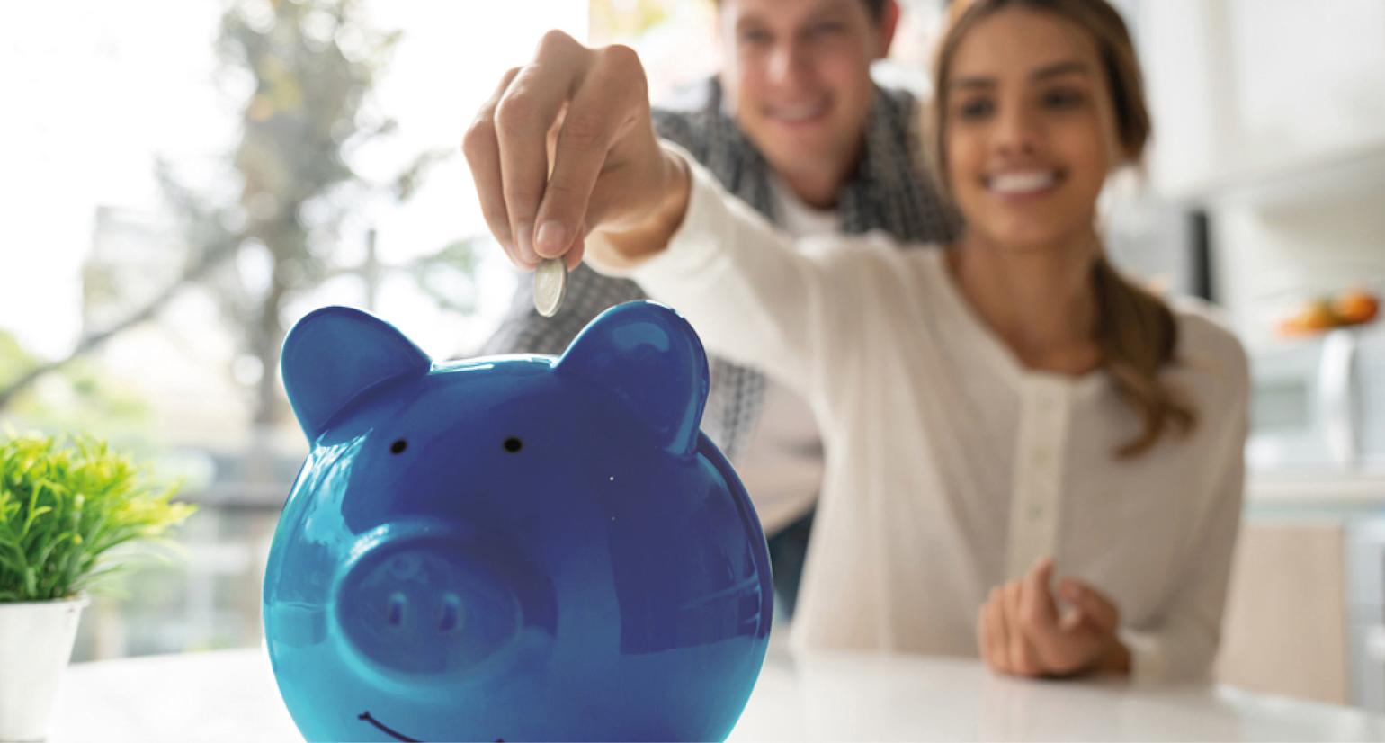 Dame putter penger på en blå sparegris og smiler.