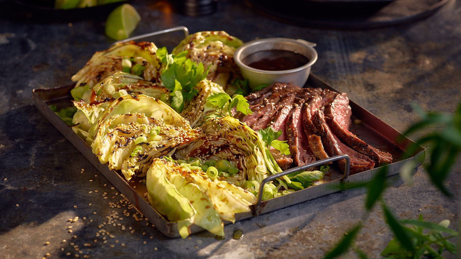 Grillet nykål og flank steak korean style med friske urter servert i mørk metallform. Liten skål saus på siden.