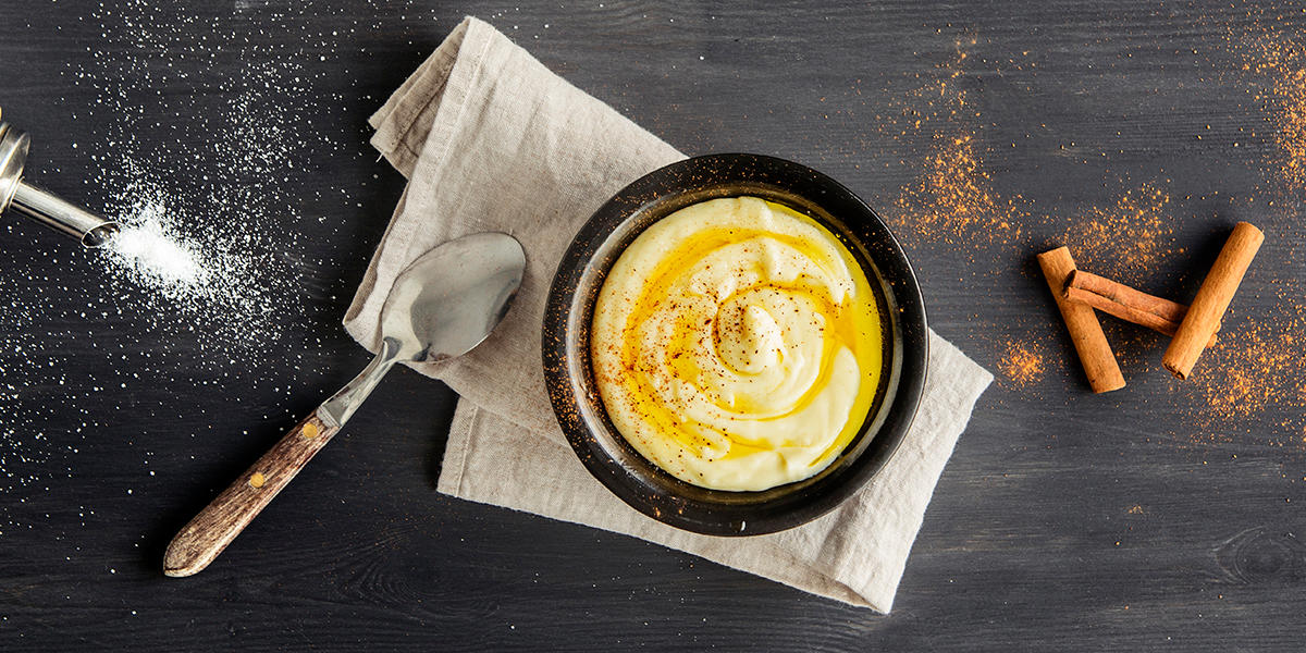 Klassisk rømmegrøt servert i svart skål på linserviett. Grøten er toppet med smeltet smør, kanel og sukker. Spiseskje, sukker og kanelstenger ved siden av.