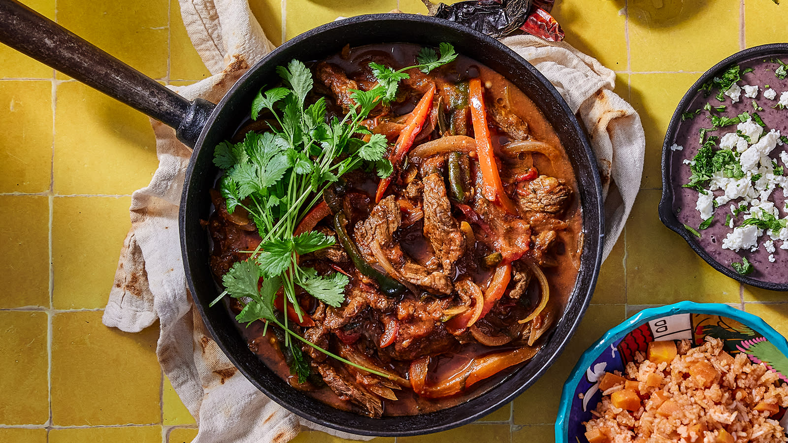 Biff a la mexicana - biff fajitas, servert i støpejernspanne med skåler av meksikansk ris og refried beans ved siden av.